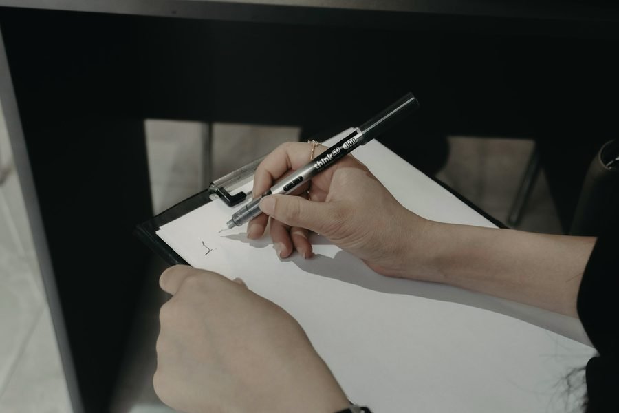 A hand writing on a clipboard with a pen.