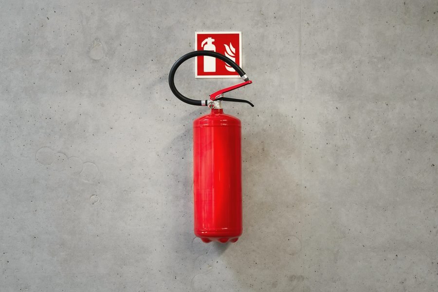 A red extinguisher hanging under a fire extinguisher sign on a bare concrete wall.
