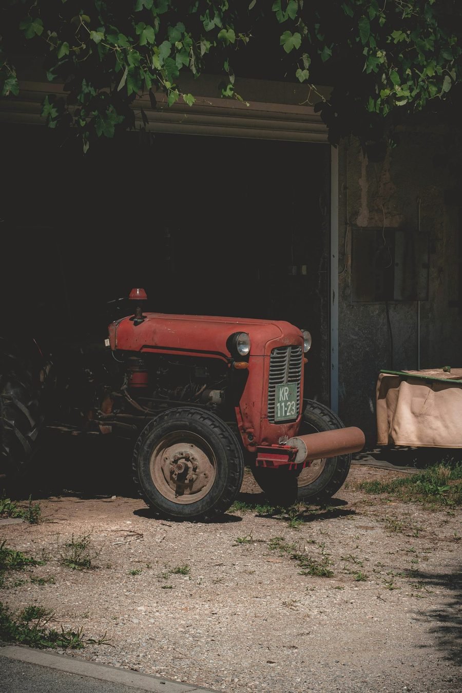 An old red tractor parked in the dark doorway of a shed.