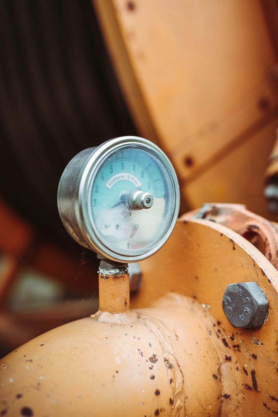 A round pressure gauge with a pale blue face on an orange metal fitting.