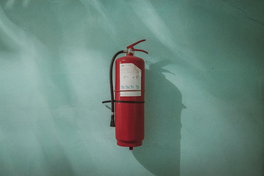 A single red extinguisher hanging on a painted teal wall, lit from one side.