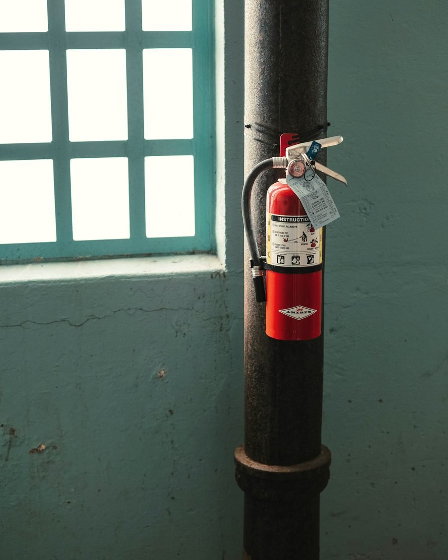 An extinguisher strapped to a black column beside a window with a green frame.